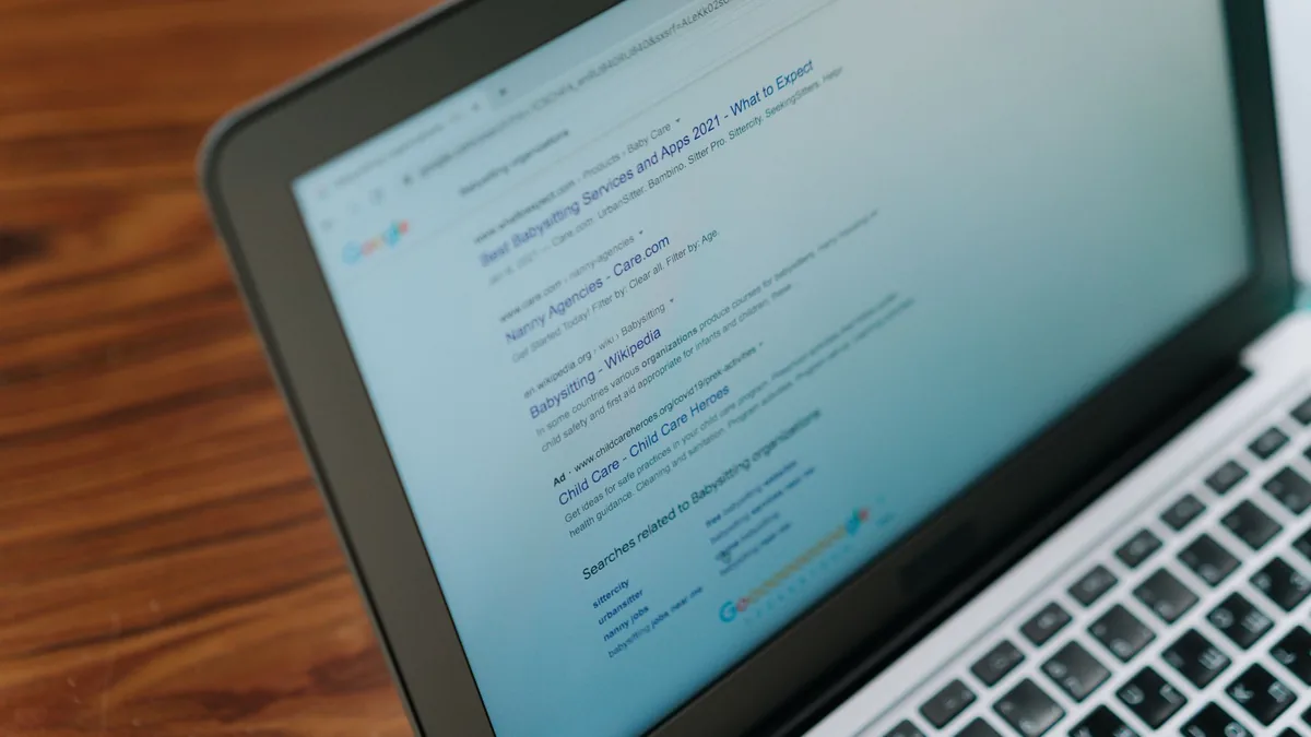 A laptop on a desk showing a search engine, hands typing